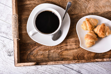 Cup of coffee on wooden tray with croissants.