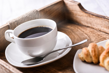 Cup of coffee on wooden tray with croissants.