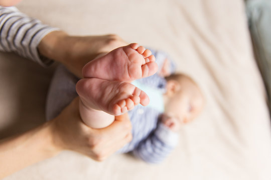 Closeup of baby feet and human hands holding kid legs. Cute little child in home interior. Healthy skin or baby care concept