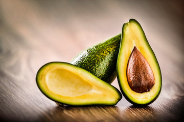 Avocado on old wooden table.Halfs on wooden bowl. Fruits healthy food concept.