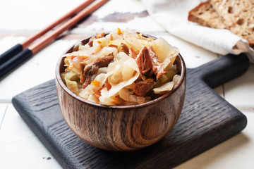 Stewed cabbage with meat in a wooden bowl on a wooden background. Traditional Russian dish of Solyanka.