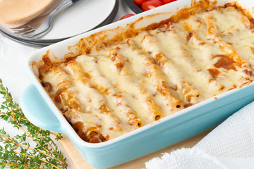 Cannelloni pasta with filling of ground beef, tomatoes, baked with bechamel tomato sauce and mozzarella. Classical Italian cuisine, white tablecloth with embroidery, rustic style, side view