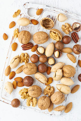 Mix of nuts - walnut, almonds, pecans, macadamia and knife for opening shell on white wooden cutting board. Healthy vegan food. Clean eating, balanced diet. Top view, macro, close up