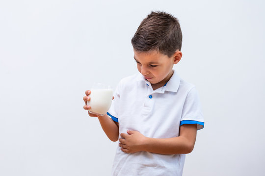 Little Boy With Dairy Allergy Holding Glass Of Milk Indoors. Child With Painful Expression After Drinking Milk. Lactose Intolerance.