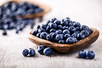 Freshly picked blueberries in wooden bowl on white table. Juicy and fresh blueberry with green leaves at rustic board. Bilberry antioxidant healthy forest food.