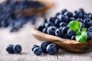 Freshly picked blueberries in wooden bowl on white table. Juicy and fresh blueberry with green leaves at rustic board. Bilberry antioxidant healthy forest food.