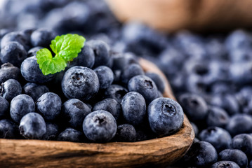 Freshly picked blueberries in wooden bowl on white table. Juicy and fresh blueberry with green leaves at rustic board. Bilberry antioxidant healthy forest food.