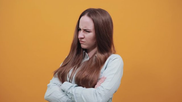 Unhappy attractive caucasian lady wearing fashion shirt isolated on orange background in studio keeping hands crossed on chest, looking at camera, angry. People emotions, lifestyle concept.