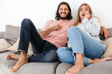 Scared young loving couple on sofa watch tv