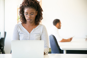 Obraz premium Front view of focused beautiful worker typing on laptop. Thoughtful young woman with dreadlocks working with laptop at office. Technology concept