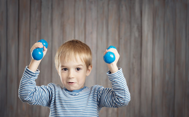 Child holding dumbbells indoors on wooden background.