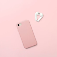 Smartphone and wireless headphones in shape of heart on bright pink background