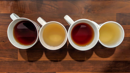 Top view of colorful teas filled in white cups and placed on wooden counter in the kitchen, served and ready to drink