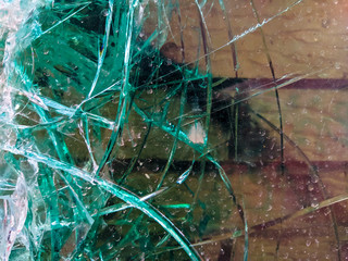Extremely damaged and broken glass in green color during an accident or a fight where the window was smashed and cracks are visible