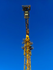 Obraz premium High yellow crane as seen from the ground with blue sky in the background on the construction site for building and doing renovations on high altitude