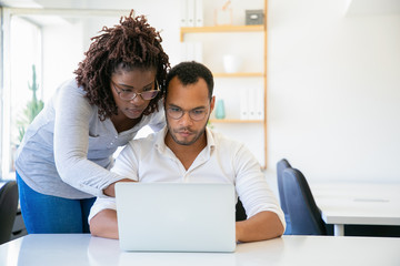Concentrated African American woman pointing at laptop. Focused colleagues working with laptop at office. Teamwork concept