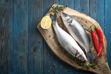 Fresh seabass and ingredients for cooking. Raw fish seabass with lemon, spices and herbs on blue wooden rustic table. Top view with copy space .