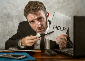 business lifestyle portrait of depressed and overwhelmed attractive man working at office computer desk in stress holding notepad as help sign feeling frustrated and exhausted