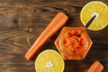 Homemade carrot jam with orange in glass jar on brown wooden background. Healthy sweet sauce, top view