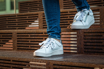 Female legs wearing jeans and white sneakers walking down on stairs 