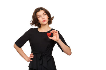 A beautiful brunette girl in a black dress on a white background holds a red decorative heart in her hands