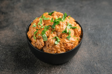 Chicken tikka masala traditional Asian spicy meat food with rice tomatoes and cilantro in a black bowl on dark background.