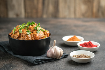 Chicken tikka masala traditional Asian spicy meat food with rice tomatoes and cilantro in a black bowl on dark background. - obrazy, fototapety, plakaty