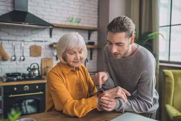 Young handsome man in grey shirt attaching smartwatch to his moms hand