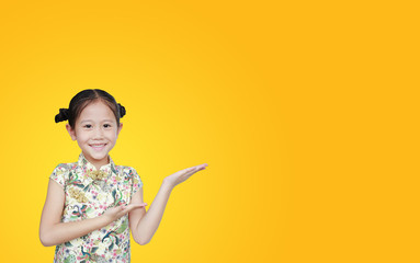 Beautiful Asian little girl wearing cheongsam with smiling and welcome gesture celebrating for happy Chinese New Year isolated over yellow background with copy space.