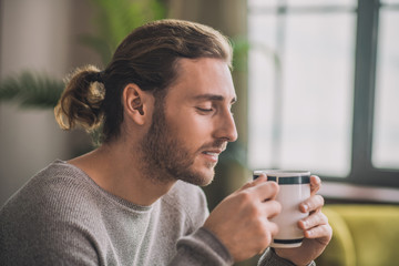 Young bearded handsome man in grey having coffee