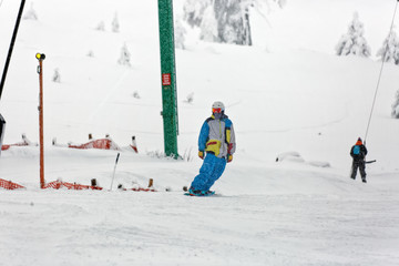 Snowboarder man with colorful outfit riding on piste on a snowy cold day on the first day of the new year. T-bar lift on the background. Kartalkaya, Turkey.