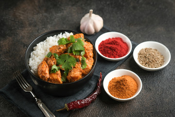 Chicken tikka masala traditional Asian spicy meat food with rice tomatoes and cilantro in a black bowl on dark wooden background.