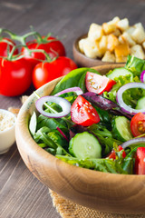 Fresh healthy salad with delicious ruccola, spinach, cabbage, arugula, feta cheese, red onion, cucumber, sesame seeds and cherry tomato on wooden background. Healthy and diet food concept.