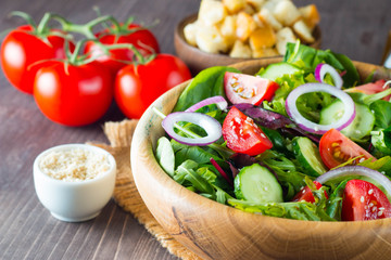 Fresh healthy salad with delicious ruccola, spinach, cabbage, arugula, feta cheese, red onion, cucumber, sesame seeds and cherry tomato on wooden background. Healthy and diet food concept.