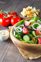 Fresh healthy salad with delicious ruccola, spinach, cabbage, arugula, feta cheese, red onion, cucumber, sesame seeds and cherry tomato on wooden background. Healthy and diet food concept.