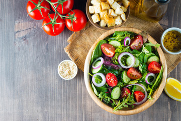 Fresh Caesar salad with delicious chicken breast, ruccola, spinach, cabbage, arugula, egg, parmesan and cherry tomato on wooden background. Oil, salt and pepper. Healthy and diet food concept.