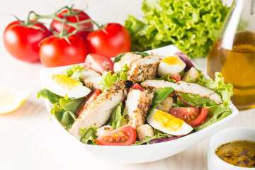 Fresh Caesar salad with delicious chicken breast, ruccola, spinach, cabbage, arugula, egg, parmesan and cherry tomato on wooden background. Oil, salt and pepper. Healthy and diet food concept.