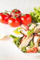 Fresh Caesar salad with delicious chicken breast, ruccola, spinach, cabbage, arugula, egg, parmesan and cherry tomato on wooden background. Oil, salt and pepper. Healthy and diet food concept.