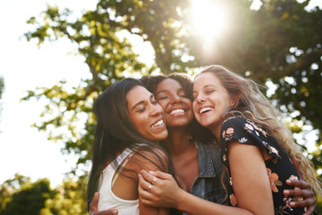 Portrait of a happy multiethnic group female friends hugging and embracing each other laughing and having fun outdoors in a park  - Powered by Adobe
