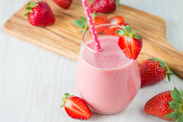 Glass of fresh strawberry milkshake, smoothie and fresh strawberries on pink, white and wooden background. Healthy food and drink concept.