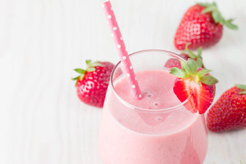 Glass of fresh strawberry milkshake, smoothie and fresh strawberries on pink, white and wooden background. Healthy food and drink concept.