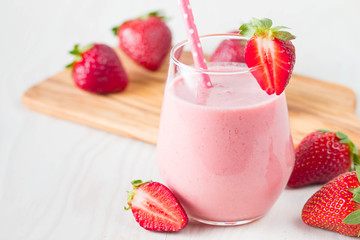 Glass of fresh strawberry milkshake, smoothie and fresh strawberries on pink, white and wooden background. Healthy food and drink concept.