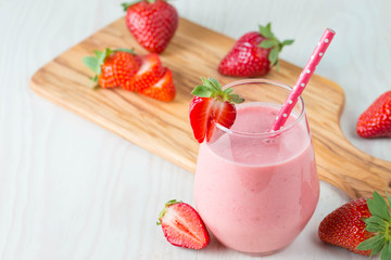 Glass of fresh strawberry milkshake, smoothie and fresh strawberries on pink, white and wooden background. Healthy food and drink concept.