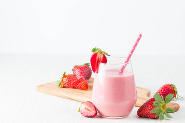 Glass of fresh strawberry milkshake, smoothie and fresh strawberries on pink, white and wooden background. Healthy food and drink concept.