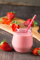 Glass of fresh strawberry milkshake, smoothie and fresh strawberries on pink, white and wooden background. Healthy food and drink concept.