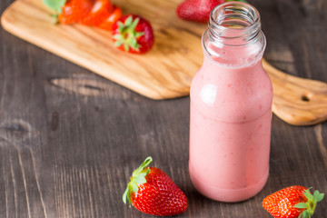 Glass of fresh strawberry milkshake, smoothie and fresh strawberries on pink, white and wooden background. Healthy food and drink concept.