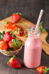 Glass of fresh strawberry milkshake, smoothie and fresh strawberries on pink, white and wooden background. Healthy food and drink concept.