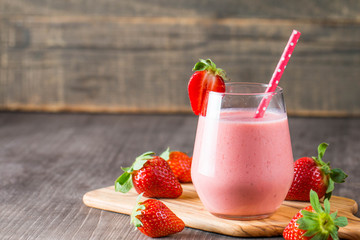 Glass of fresh strawberry milkshake, smoothie and fresh strawberries on pink, white and wooden background. Healthy food and drink concept.
