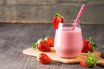 Glass of fresh strawberry milkshake, smoothie and fresh strawberries on pink, white and wooden background. Healthy food and drink concept.