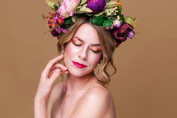 beautiful young woman model with bright flowers on her head on the ocher color background